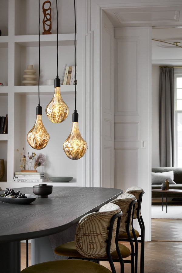 Sfeerafbeelding van drie doorzichtige gouden LED hanglampen boven eettafel